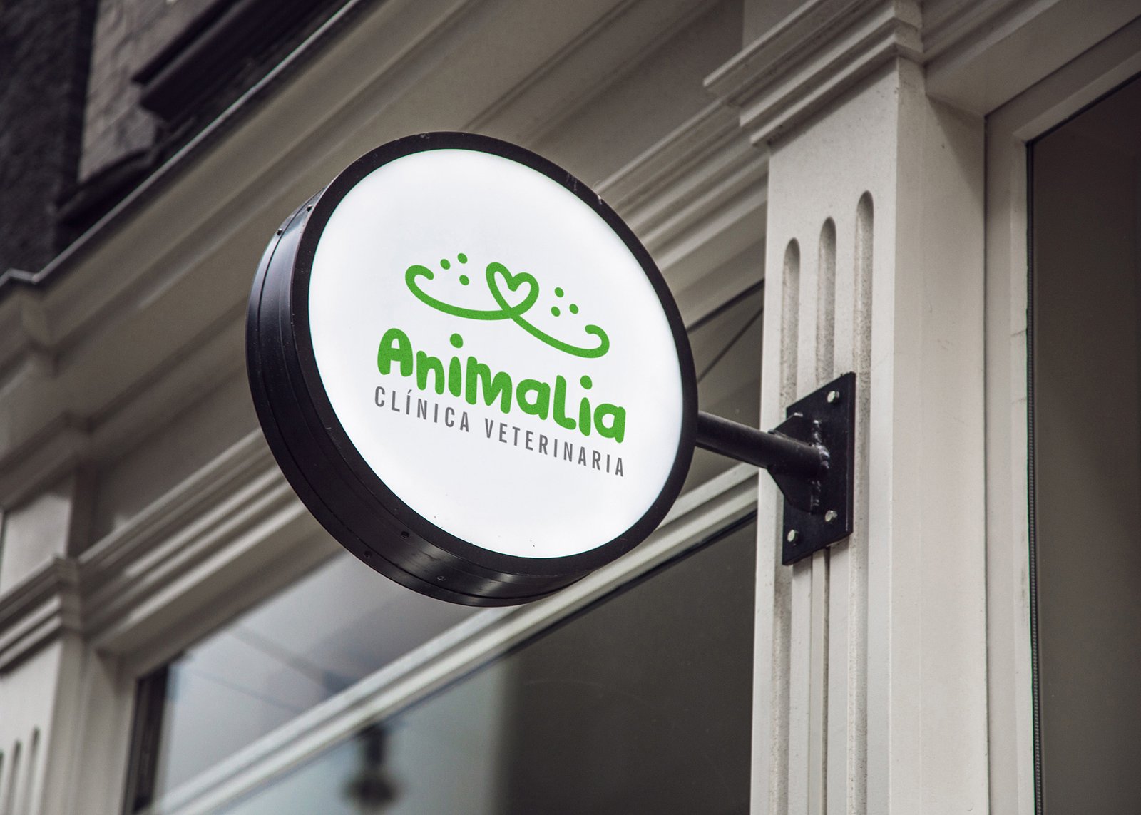 Logo Animalia - Clínica Veterinaria, montado sobre un letrero redondo que está instalado sobre un muro color crema. El logo es color verde, con icono de hocico de un perro o gato en forma de corazón.